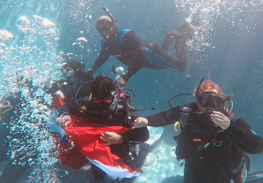 Two scuba divers underwater holding a flag — Black Tech Link BIPOC Coastal Research Program (BCRP)
