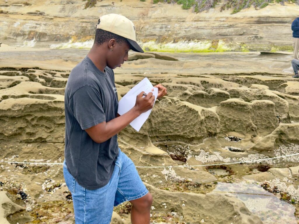 Student writing field notes at a coastal site — Black Tech Link BIPOC Coastal Research Program (BCRP)